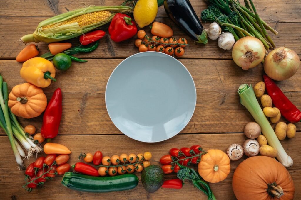Top view of assorted fresh vegetables arranged around a plate on a rustic wooden table.